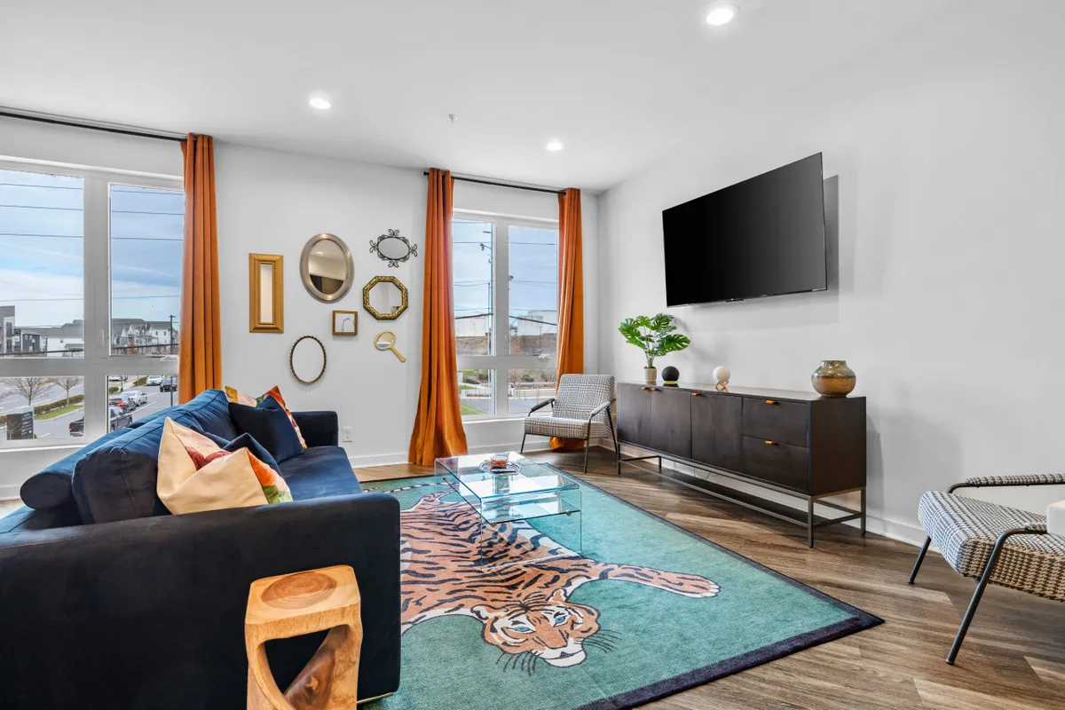 A bright, playful living room featuring a sofa, large windows letting in natural light, a prominent tiger rug, and colorful artwork on the walls. The scene suggests a welcoming spot for entertaining guests, enjoying downtime, or simply soaking in the city energy from the comfort of home.