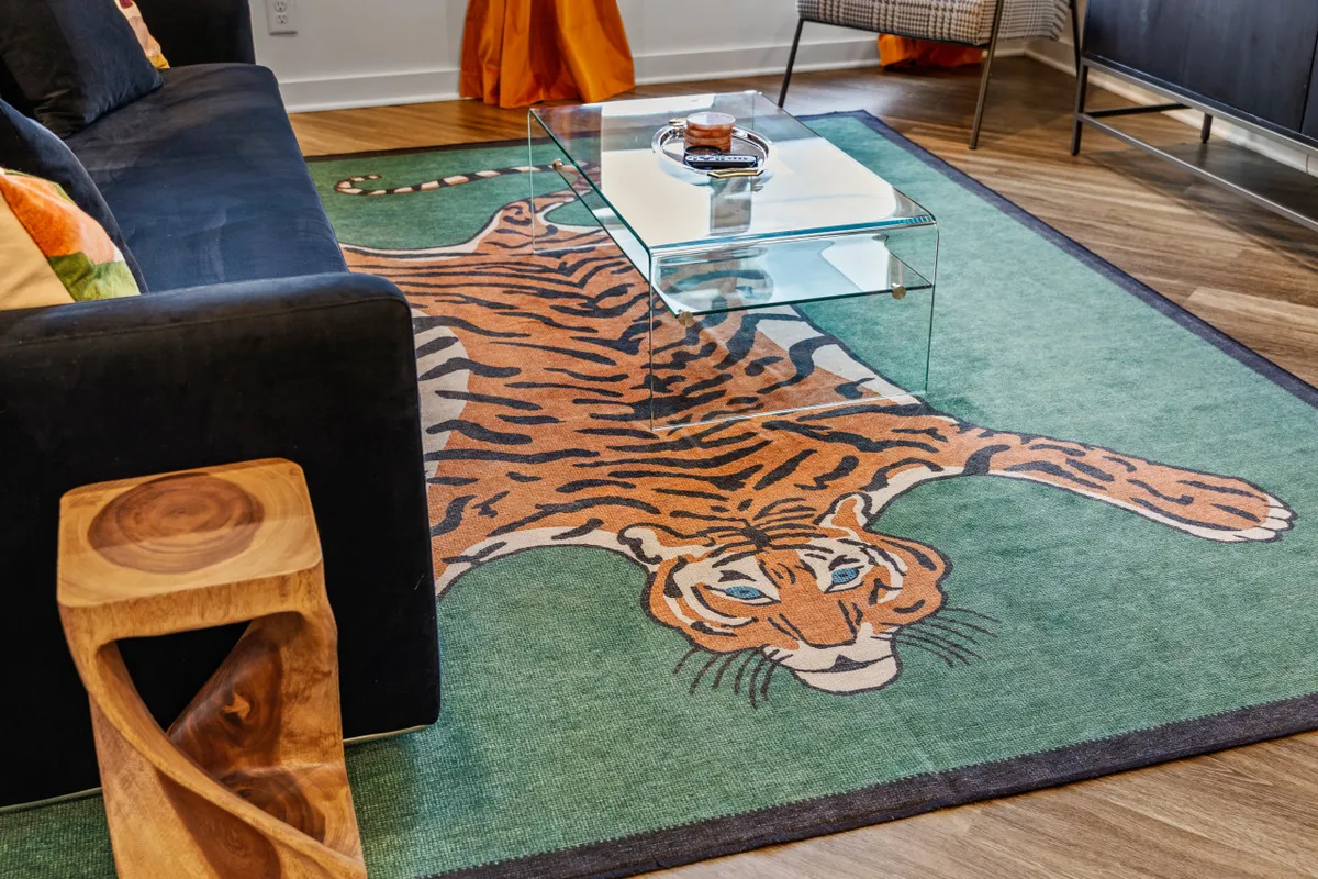 This interior image focuses on a black sofa and playful tiger rug, complemented by a glass coffee table and a wooden side table. The setup is open and inviting, providing a cozy yet lively space for friends to relax, socialize, or plan their downtown adventures.
